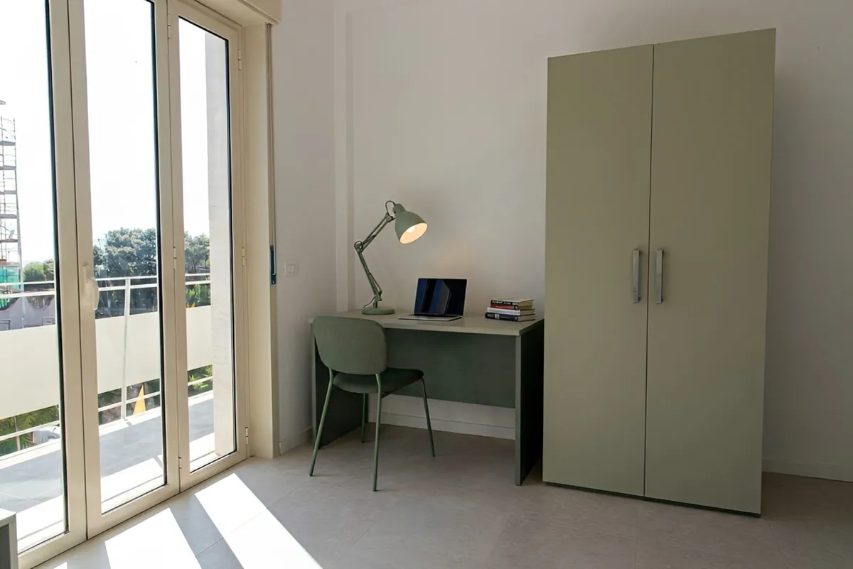 Escritorio con lámpara y silla, armario de dos puertas y puerta ventana