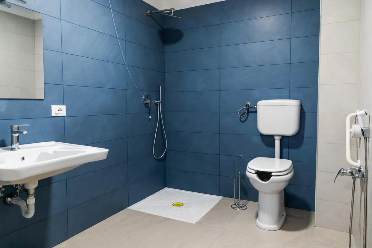 Baño con ducha a ras de suelo, lavabo, inodoro con ducha higiénica y barra de apoyo
